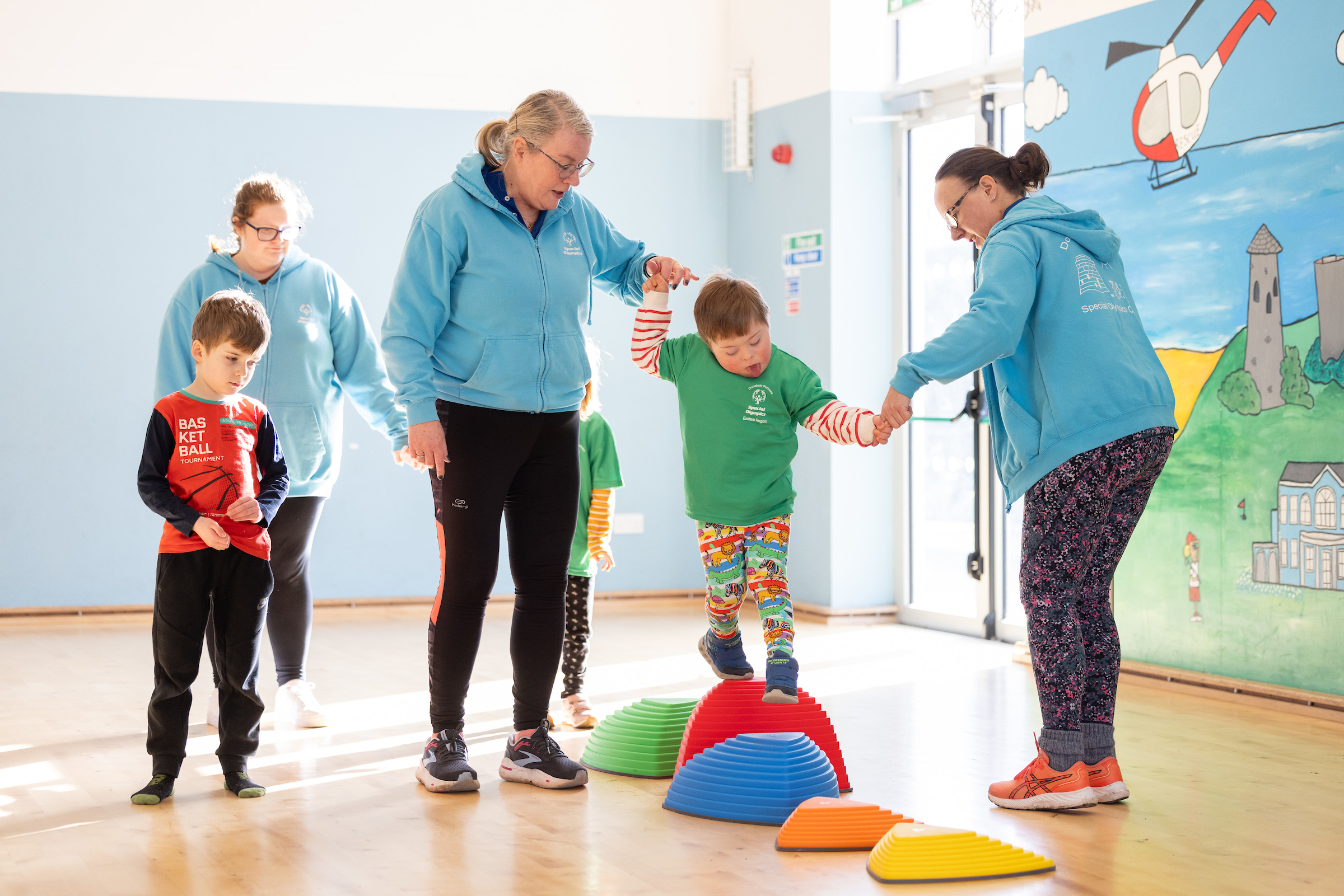 Three staff members helping two kids across balance obstacle course