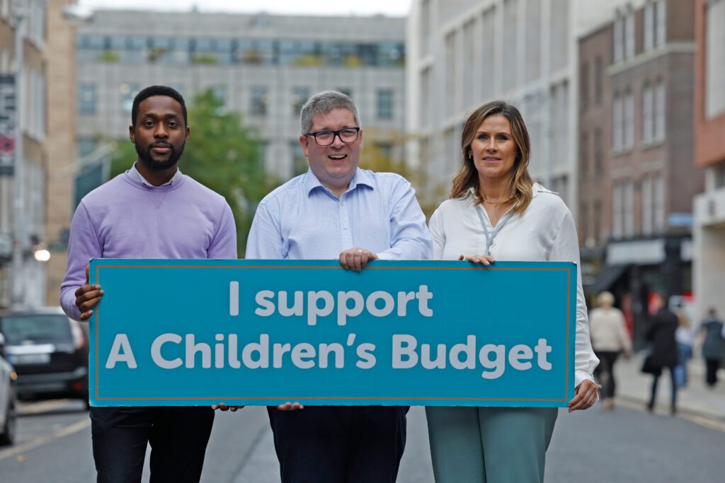 Three people in the centre of a Dublin Street. They are holding a sign 'I support a Children's Budget'. This is part of an ongoing campaign by Community Foundation Ireland partner, the Children's Rights Alliance.