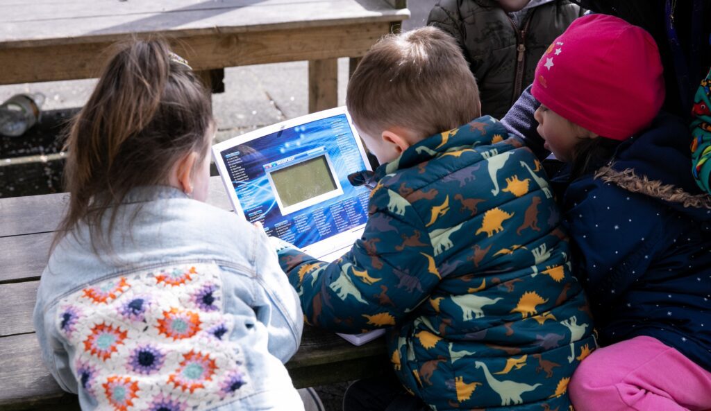 A group of three children playing with an electronic toy with their backs to the camera. The children attend a project by a partner of Community Foundation Ireland.