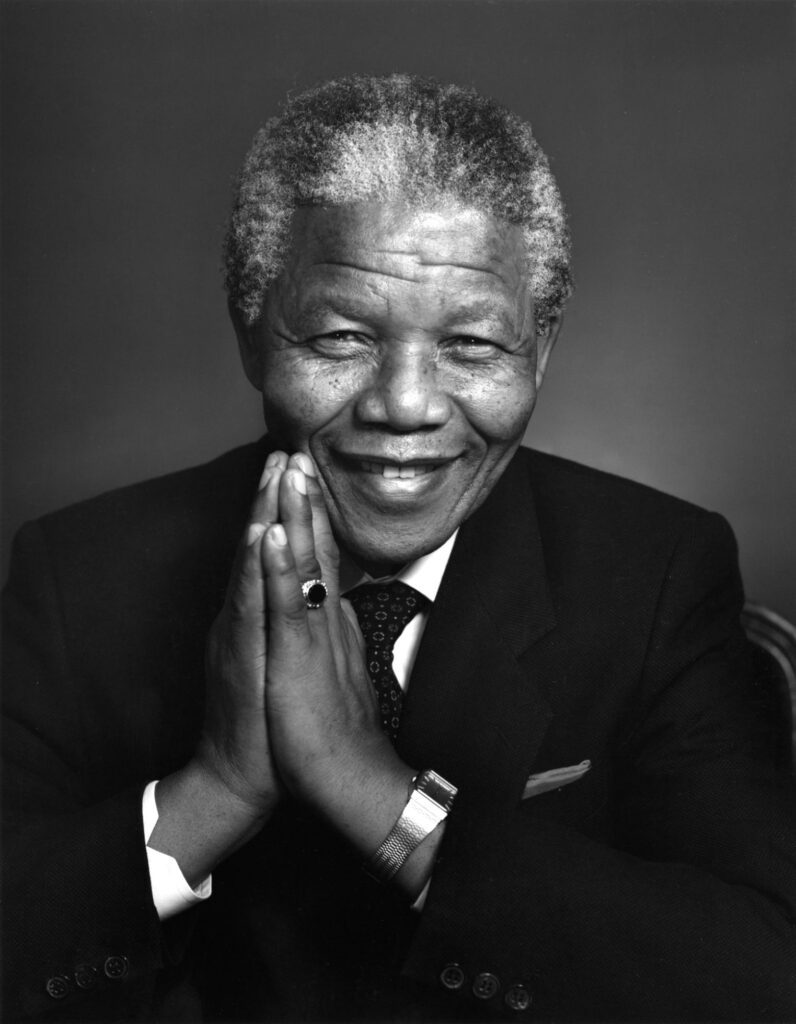 A black and white photograph of the late South African President Nelson Mandela, looking into the camera.